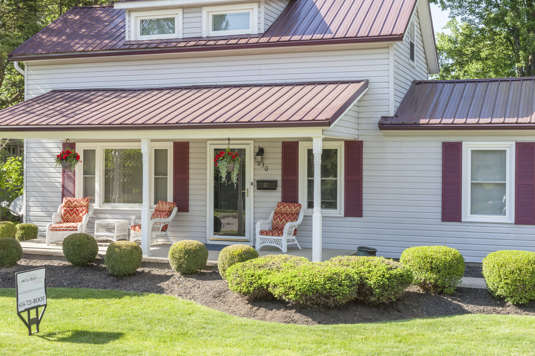 Burgundy metal roof on a white country-style home with burgundy shutters
